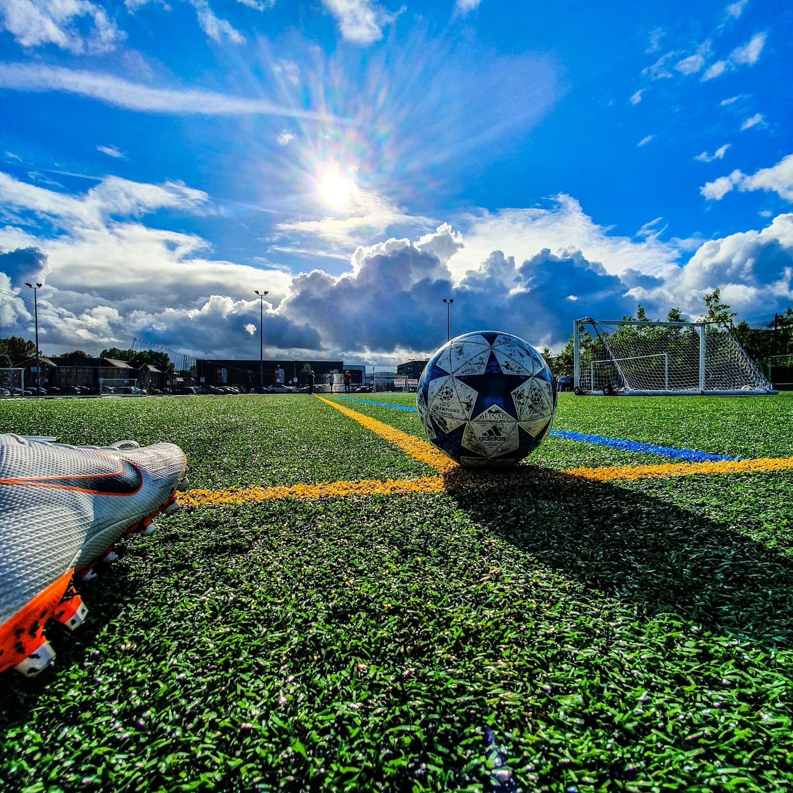 A football on an artificial pitch next to a boot, with a goal behind